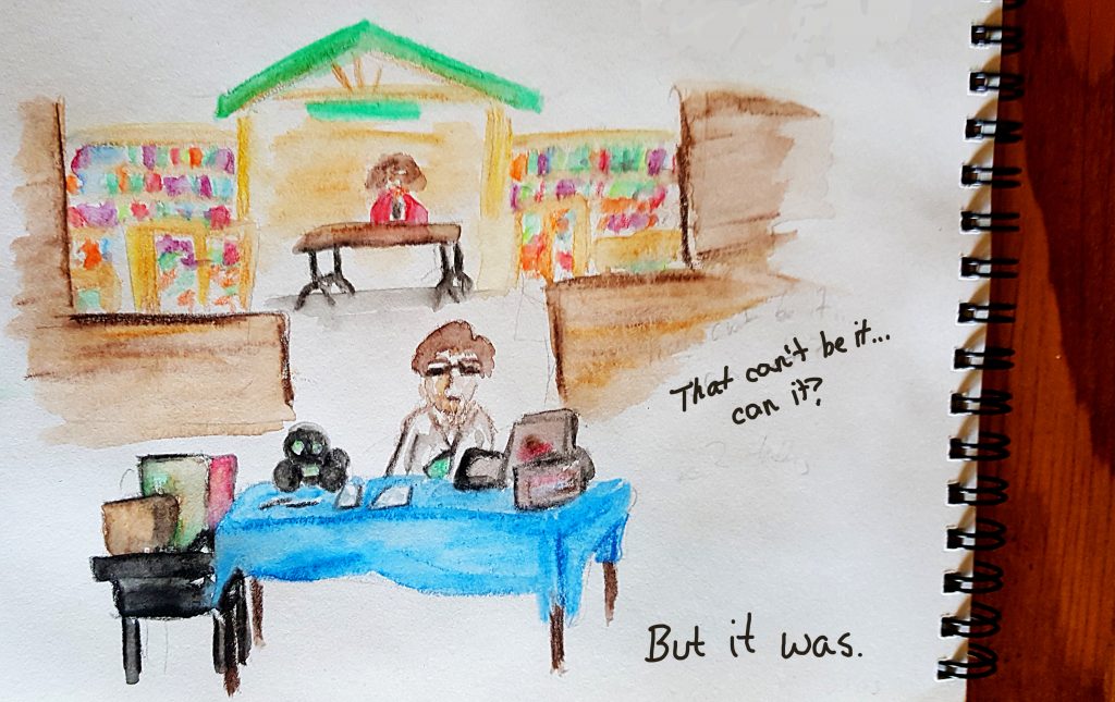 Maker Faire BN 2 tables a blue one in front staffed by a man and one in the back staffed by a person wearing red cardigan